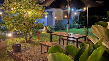 An outdoor patio area with a table and chairs, surrounded by greenery and a building in the background.