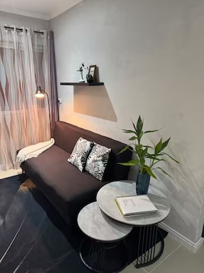 Ein modernes Wohnzimmer mit einem dunklen Sofa, einem runden Couchtisch, einer Kühlpflanze und einem an der Wand befestigten Regal mit Dekoration.