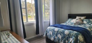 A bedroom with a bed, curtains, a window, and a small table with a plant. - Park-view private rooms in a house in Clovelly Park, Adelaide, South Australia! (Clovelly Park)