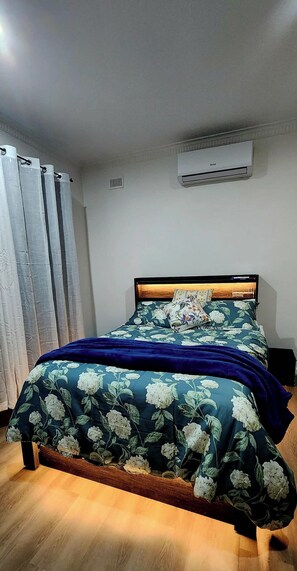 A bedroom with a bed, curtains, an air conditioning unit, and a wooden floor. - Park-view private rooms in a house in Clovelly Park, Adelaide, South Australia! (Clovelly Park)