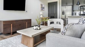 A modern living room with a sofa, a coffee table, and a TV mounted on the wall. - Landing | Amazing 1BD, Courtyard, Gym (Atlanta)