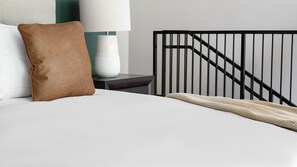 A neatly made bed with a brown pillow and a white blanket, a bedside lamp, and a black metal headboard. - Landing | Amazing 1BD, Courtyard, Gym (Atlanta)
