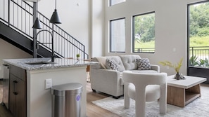 A modern living room with a grey sofa, a coffee table, and a kitchen area with a granite countertop. - Landing | Amazing 1BD, Courtyard, Gym (Atlanta)