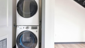 A stacked washer and dryer unit in a room with a wooden floor and white walls. - Landing | Amazing 1BD, Courtyard, Gym (Atlanta)