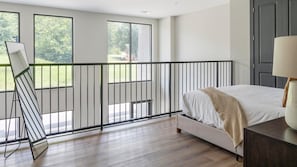 A bedroom with a bed, a nightstand, a lamp, and a balcony railing. - Landing | Amazing 1BD, Courtyard, Gym (Atlanta)