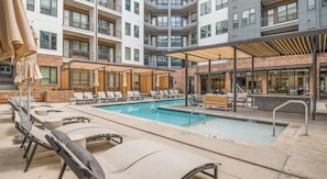 A rooftop pool area with lounge chairs and umbrellas, surrounded by a multi-story building with balconies. - Landing | Amazing 1BD, Courtyard, Gym (Atlanta)