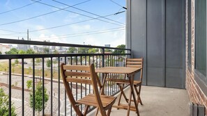 A balcony with a wooden table and chairs, a view of a cityscape, and a grey wall. - Landing | Beautiful 1BD, Gym, Courtyard (Atlanta)
