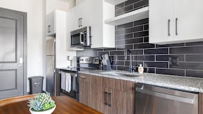 A modern kitchen with stainless steel appliances, a granite countertop, and black and white cabinetry. - Landing | Beautiful 1BD, Gym, Courtyard (Atlanta)