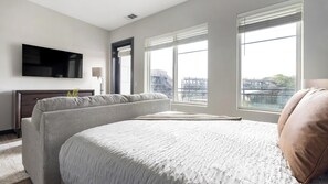 A hotel room with a large bed, a flat-screen TV mounted on the wall, and a window with a view of the cityscape. - Landing | Beautiful 1BD, Gym, Courtyard (Atlanta)