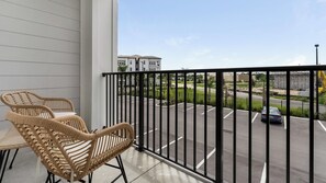 A balcony with wicker chairs, a view of a parking lot, and a building in the background. - Landing | Spectacular 2BD, Pool, Gym (Port Charlotte)
