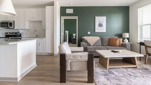 A modern living room with a sofa, a coffee table, and a kitchen area with white cabinets and a microwave. - Landing | Modern 2BD, Gym, Pool (Port Charlotte)