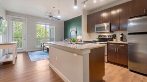 A modern kitchen with a central island, stainless steel appliances, and wooden cabinets. - Landing | Incredible 1BD, Gym, Pool (Austin)