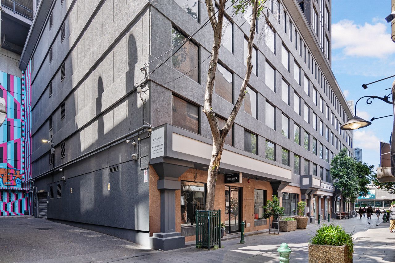 A modern building with a glass facade, a storefront, and a tree in front.