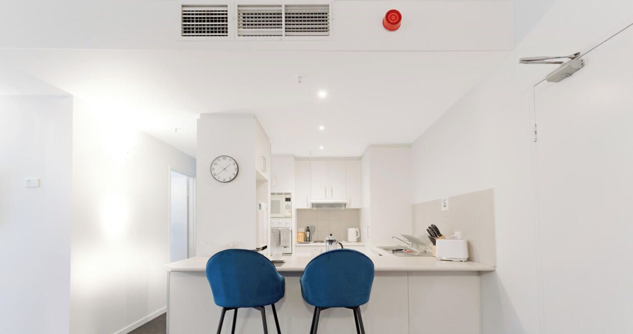 A modern kitchen with white cabinets, a microwave, and a clock on the wall.