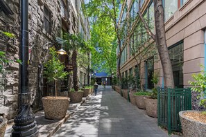 A narrow urban street lined with trees and planters, leading to a building with a blue roof. - Large 2-bedroom on Flinders (Melbourne)