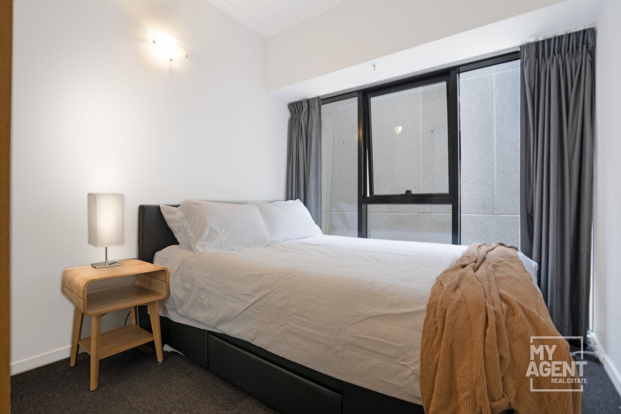 A bedroom with a bed, a bedside table with a lamp, a window with curtains, and a view of the outside.
