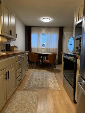 Une cuisine compacte avec un coin repas, des meubles en bois, un four encastré et une fenêtre avec des rideaux.
