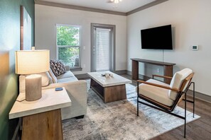 A modern living room with a sofa, coffee table, and armchair. A flat-screen TV is mounted on the wall. - Landing | Stylish 2BD, Gym (Destin)