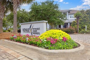 Schild für 'Emerald Coast Apartments' mit einem angelegten Garten mit verschiedenen Pflanzen und Blumen.