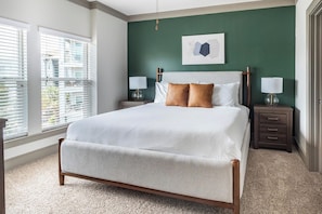 Un dormitorio con una cama grande, dos mesitas de noche, una ventana con persianas y una pared verde decorativa.