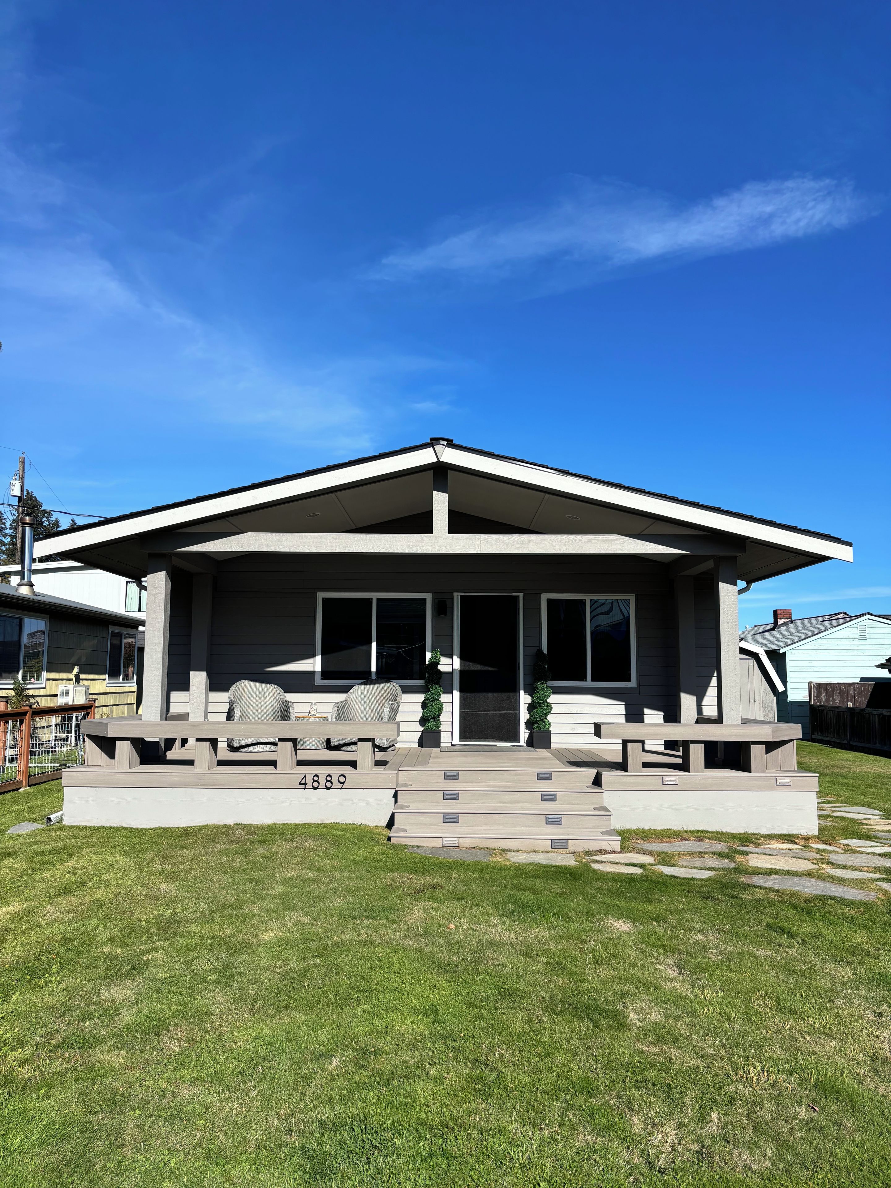 A modern house with a covered patio, a number '4889' on the steps, and a clear blue sky.