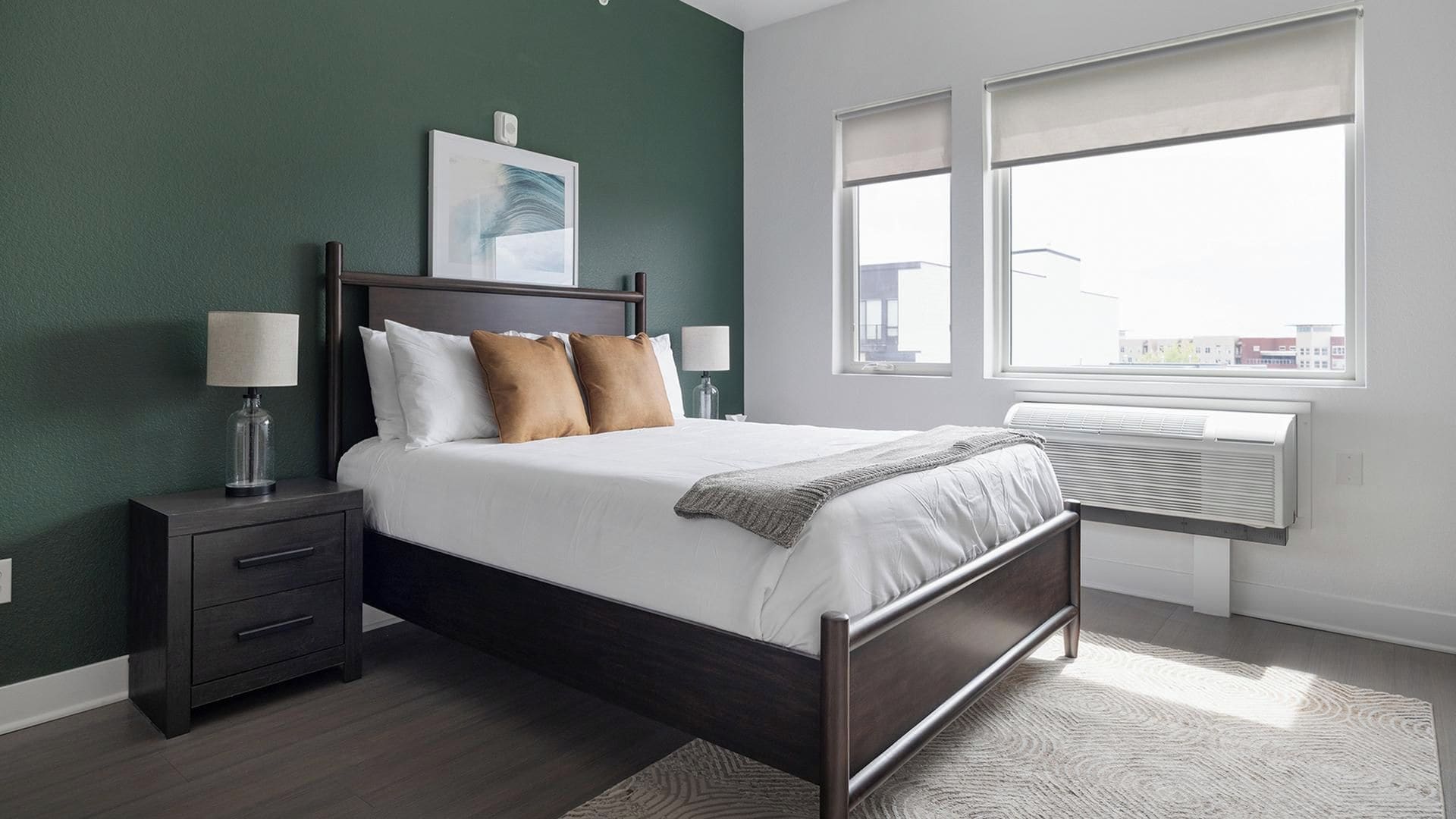 A modern bedroom with a bed, bedside tables, a window, and an air conditioning unit.