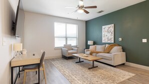 A living room with a sofa, coffee table, and a TV mounted on the wall. - Landing | Stunning 2BD, Rooftop Lounge, Clubhouse (Fort Worth)