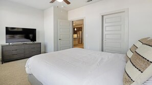 A bedroom with a bed, a TV on a dresser, and two doors leading to other rooms. - Landing | Stylish 1BD, Clubhouse, Rooftop Lounge (Fort Worth)