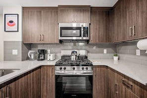 A modern kitchen with wooden cabinets, stainless steel appliances, and a stainless steel range hood. - Corner Glen Retreat | 6BR | Sleeps 12 - Holiday Home (Calgary)