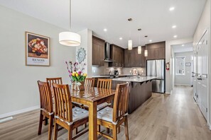 A modern kitchen with wooden cabinets, a central island, and pendant lighting. - Corner Glen Retreat | 6BR | Sleeps 12 - Holiday Home (Calgary)
