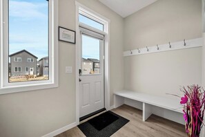 A hallway with a door leading to a residential area, a bench, and a coat rack. - Corner Glen Retreat | 6BR | Sleeps 12 - Holiday Home (Calgary)