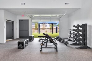 A gym with weightlifting equipment, a bench, and a squat rack. - Landing | Modern 1BD, Yoga Studio, Gym (Huntsville)