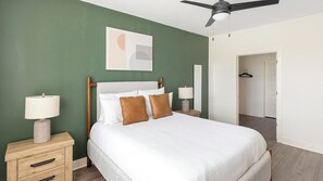 A hotel room with a bed, bedside tables, a ceiling fan, and a door leading to another room. - Landing | Modern 1BD, Game Room, Gym (Huntsville)