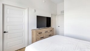 A bedroom with a bed, a dresser, a television, and white doors. - Landing | Beautiful 2BD, Yoga Studio, Game Room (Huntsville)