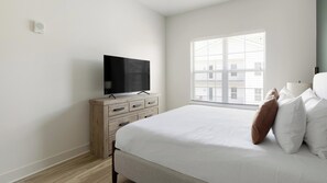 Een slaapkamer met een bed, een tv op een houten dressoir, een raam met zonwering en uitzicht op de stad.