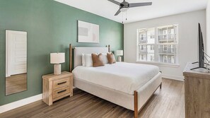 Ein Schlafzimmer mit Bett, Nachttischen, Deckenventilator, Fenster mit Jalousien und einer Tür.
