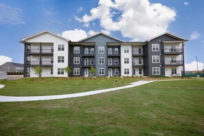A multi-story residential building with a flat roof, balconies, and a well-maintained lawn. - Landing | Amazing 2BD, Game Room, Gym (Huntsville)