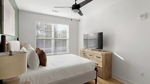 A bedroom with a bed, bedside lamp, TV, and a ceiling fan. - Landing | Amazing 2BD, Game Room, Gym (Huntsville)