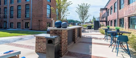 Un área de patio al aire libre con edificios de ladrillo, mobiliario exterior y una parrilla.