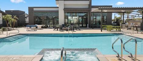 A swimming pool with a hot tub, lounge chairs, and a covered seating area.