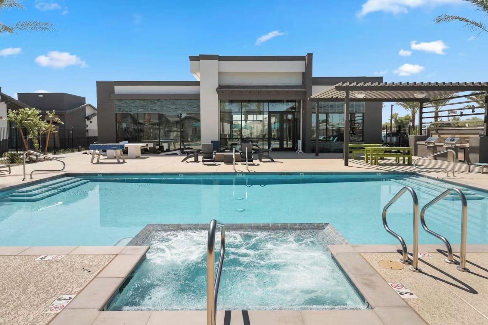 A swimming pool with a hot tub, lounge chairs, and a covered seating area.