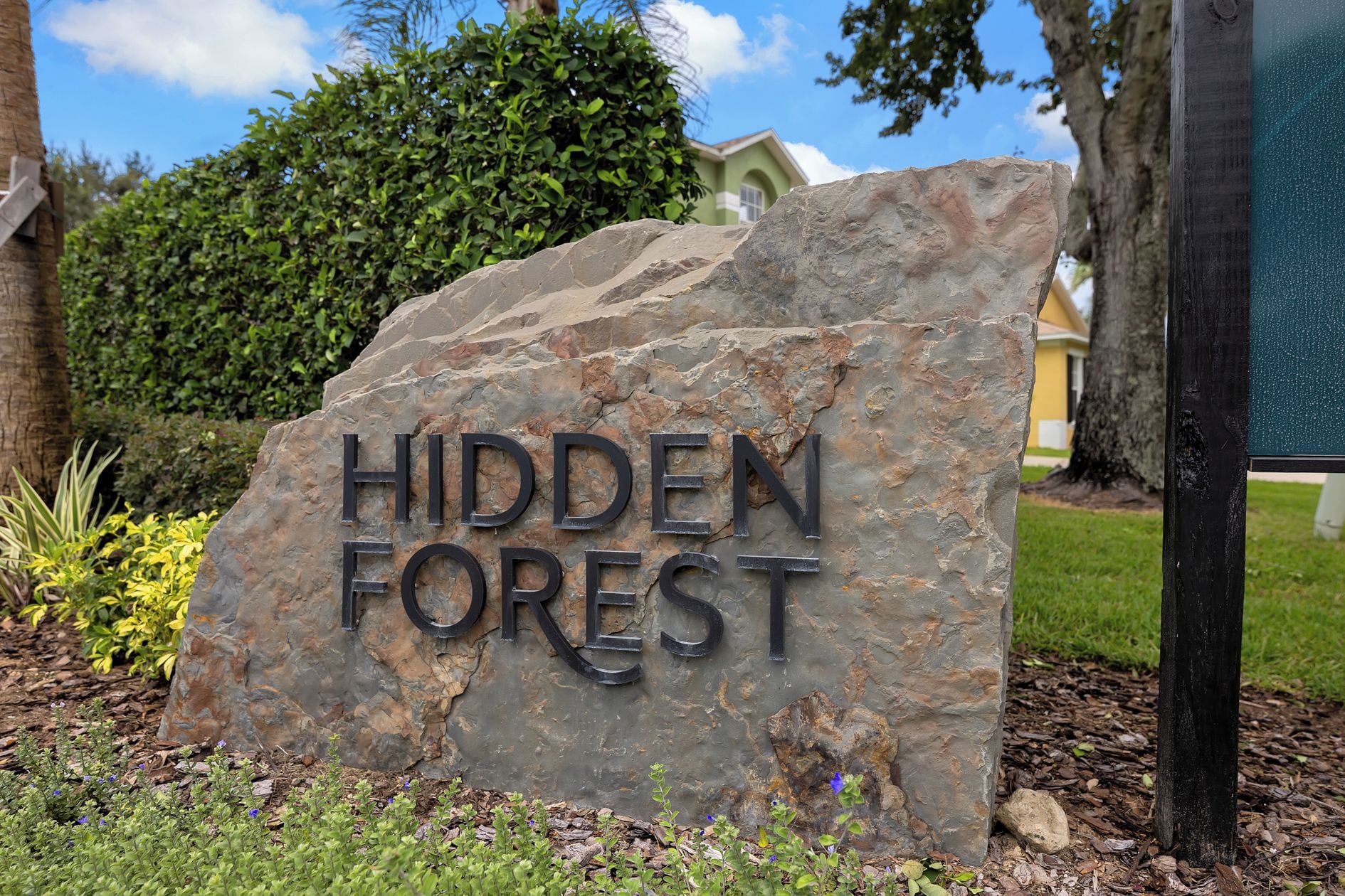A stone sign with the words 'HIDDEN FOREST' indicating a location or property name.