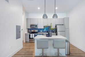 A modern kitchen with a central island, stainless steel appliances, and pendant lighting. - Landing | Incredible 1BD, Pool (West Hartford)