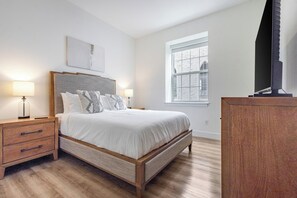 A bedroom with a bed, bedside tables, a dresser, a window, and a wall-mounted artwork. - Landing | Beautiful 1BD, Pool (West Hartford)