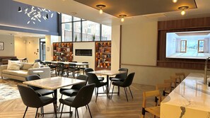 Een moderne zithoek met een bank, eettafels, stoelen, boekenkasten en een groot scherm waarop een stadsbeeld te zien is.