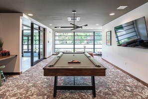 A pool table in a room with large windows, a ceiling fan, and a view of greenery outside. - Landing | Beautiful 1BD, Pool (West Hartford)