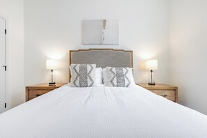 Een opgemaakt bed met een witte dekbedovertrek en twee nachtkastjes met lampen.