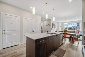 A modern kitchen with a central island, pendant lighting, and a view to the living area. - Corner Glen Retreat | 4BR Upper | Sleeps 8 - Holiday Home (Calgary)
