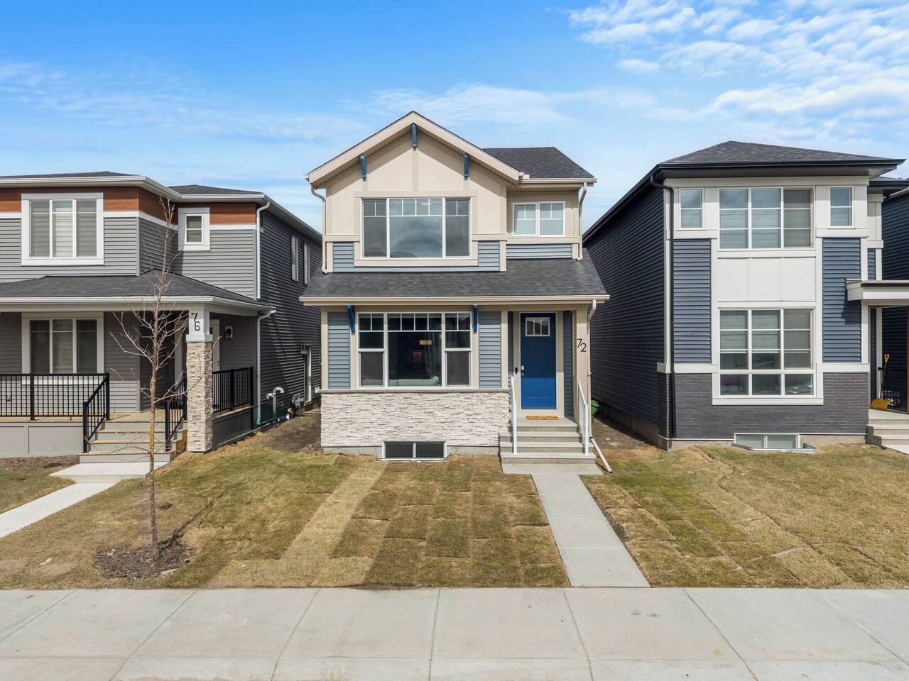 A two-story residential building with a stone facade, a blue front door, and a small front yard.