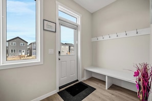 A hallway with a door leading to a residential area, a bench, and a coat rack. - Corner Glen Retreat | 4BR Upper | Sleeps 8 - Holiday Home (Calgary)